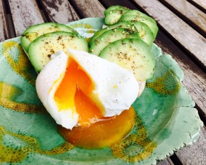 oeuf poché présenté avec deux tartines de tranches d'avocat parsemées d'huile d'olive, fleur de sel, thym en poudre et graines de sésame